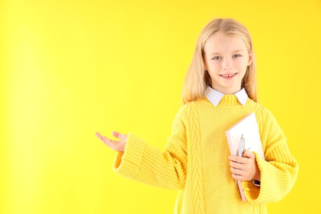 Niña linda con cuaderno y bolígrafo sobre fondo amarillo