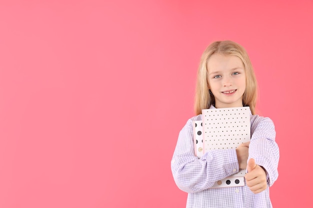 Niña linda con cuadernos sobre fondo rosa