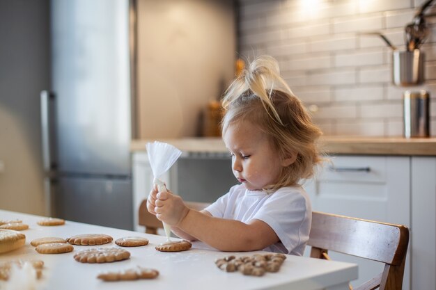 Niña linda decora pan de jengibre con preparación de glaseado de azúcar para el concepto de Navidad