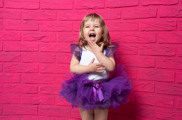 Niña linda despreocupada en falda de tutú riendo tapándose la boca con la mano en rosa