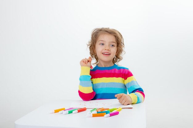 Una niña linda dibuja en la mesa con lápices aislados en un fondo blanco