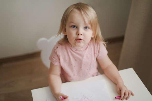 Una niña linda dibuja en la mesa con lápices