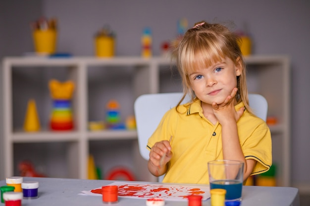 Niña linda dibuja con pinturas en kindergarten.