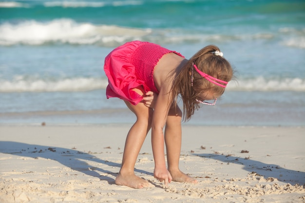 Niña linda dibuja sobre la arena blanca en la playa tropical