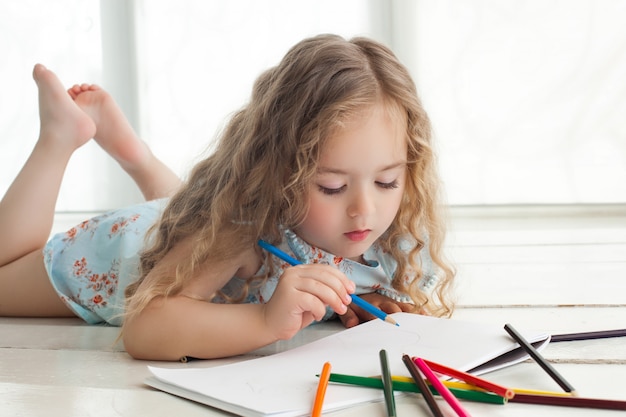 Niña linda dibujo con lápices de colores sobre papel. Bastante pequeño niño dibujando en el interior. Adorable artista