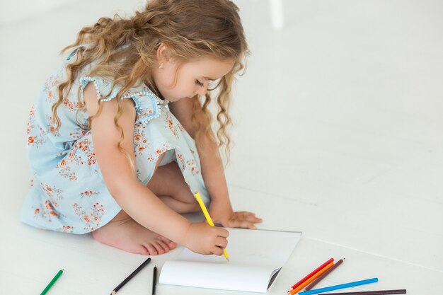 Niña linda dibujo con lápices de colores sobre papel. Bastante pequeño niño dibujando en el interior. Adorable artista