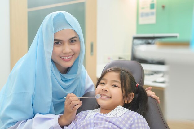 Una niña linda con los dientes examinados por un dentista musulmán en el chequeo dental de la clínica dental y el concepto de dientes sanos