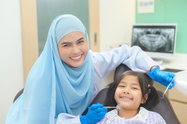 Una niña linda con los dientes examinados por un dentista musulmán en los dientes de la clínica dental