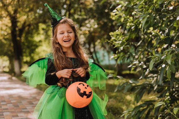 Niña linda en un disfraz verde de Halloween de una bruja o hada con una canasta de calabaza para dulces