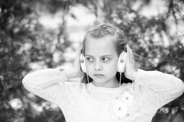 Niña linda disfrutando de la música con auriculares en el día de verano