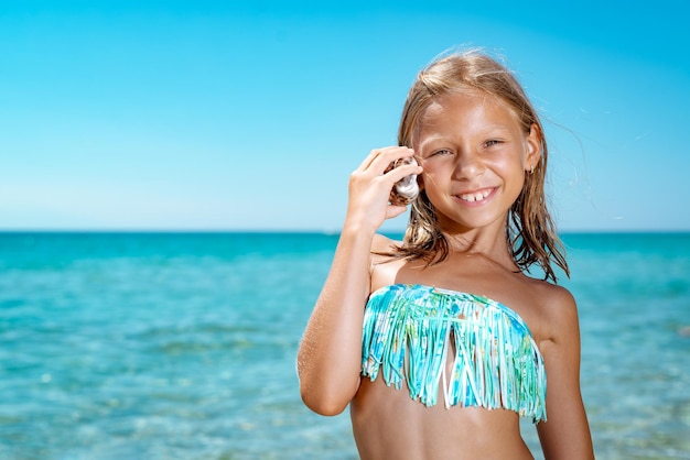 Niña linda disfrutando en la playa. Ella está posando y mirando a la cámara con una sonrisa en su rostro.