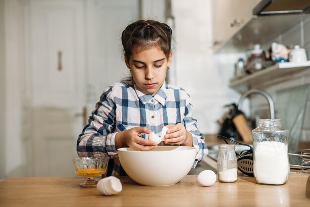 Niña linda divertida que prepara la masa en la cocina. Niño hornea galletas en la cocina de casa.