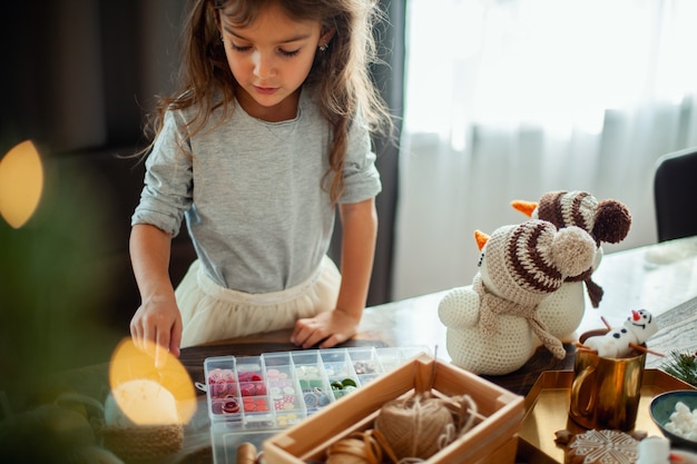 Niña linda elige botones para muñecos de nieve tejidos decoración de año nuevo está sobre la mesa preparación para ...