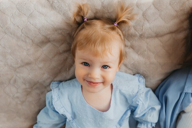 Niña linda se encuentra en la cama y sonríe. vista desde arriba. retrato de un niño