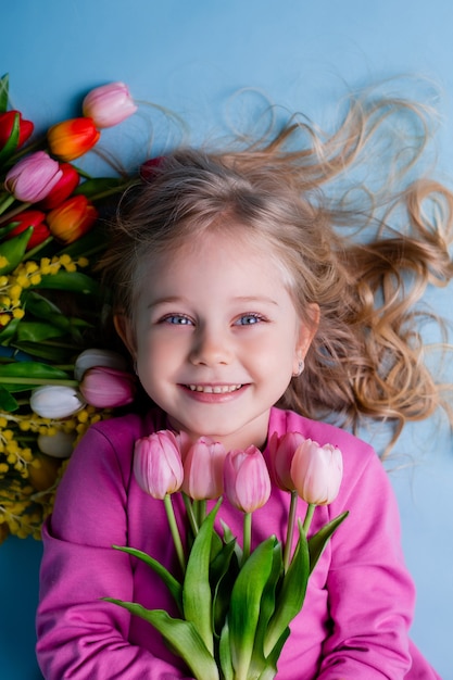 Una niña linda se encuentra entre los tulipanes sobre un fondo azul en el estudio.