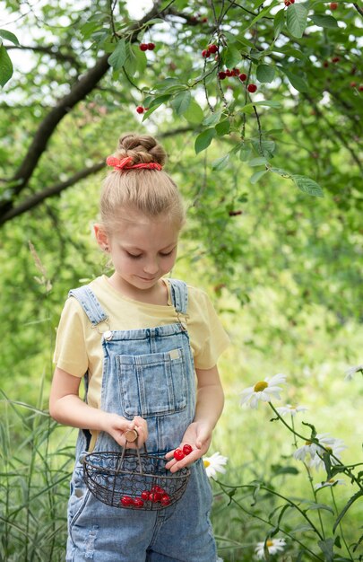 Niña linda escoge una cereza de un árbol en el jardín de cerezos