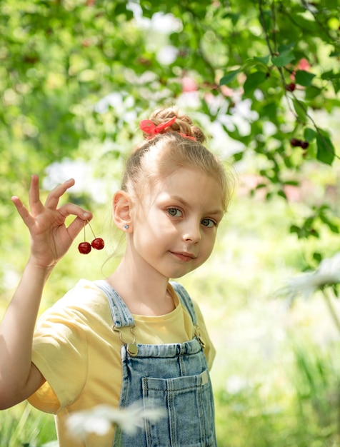 Niña linda escoge una cereza de un árbol en el jardín de cerezos