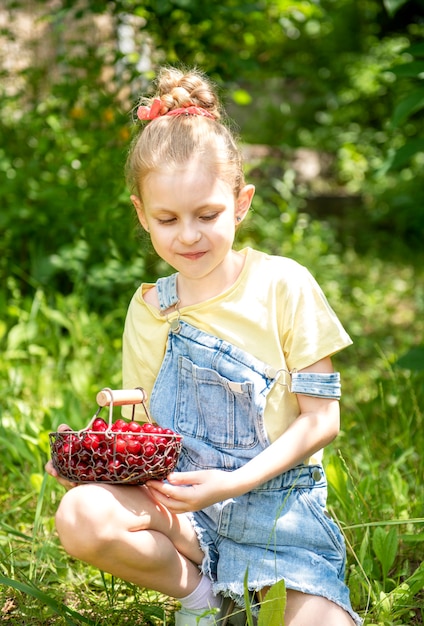 Niña linda escoge una cereza de un árbol en el jardín de cerezos