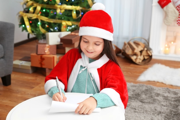 Niña linda escribiendo una carta a Santa Claus en la mesa