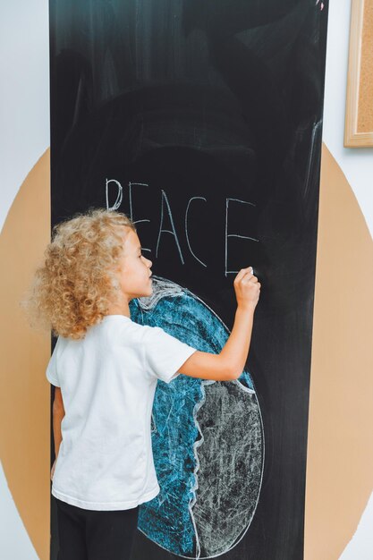 Foto una niña linda se para con la espalda y dibuja un planeta en el tablero el niño sostiene sus manos como una casa por encima del planeta