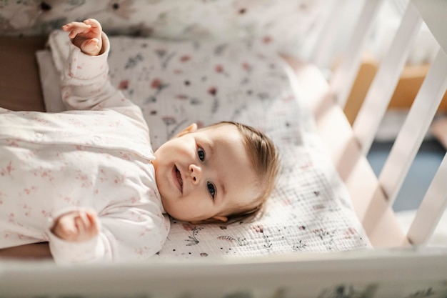 Una niña linda está acostada en su cuna y sonriendo a la cámara