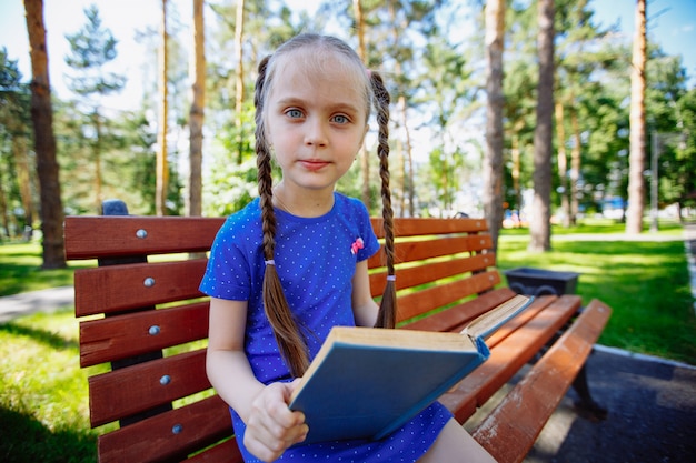 Niña linda está sentada en un banco y está leyendo un libro
