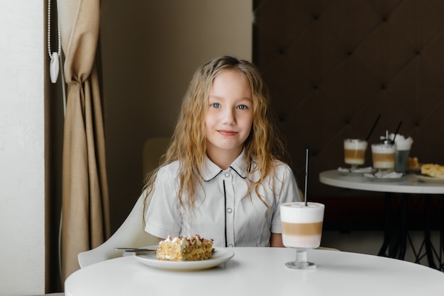 Una niña linda está sentada en un café y mirando un pastel y primer plano de cacao. Dieta y nutrición adecuada.