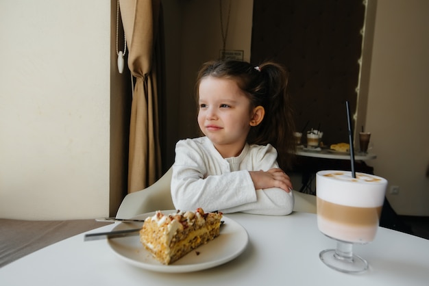 Una niña linda está sentada en un café y mirando un pastel y primer plano de cacao. Dieta y nutrición adecuada.