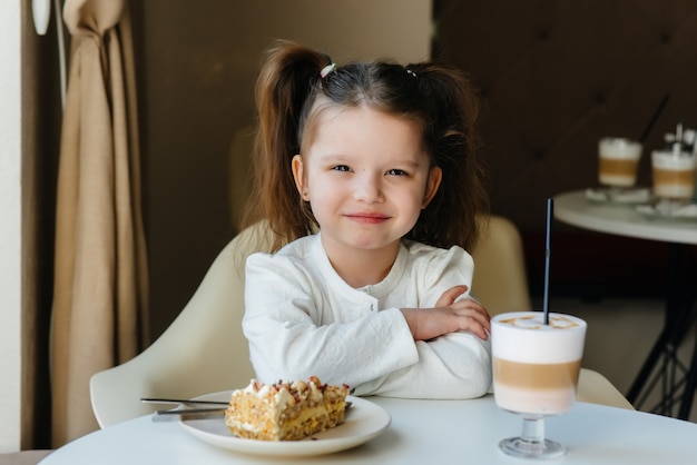 Una niña linda está sentada en un café y mirando un pastel y primer plano de cacao.