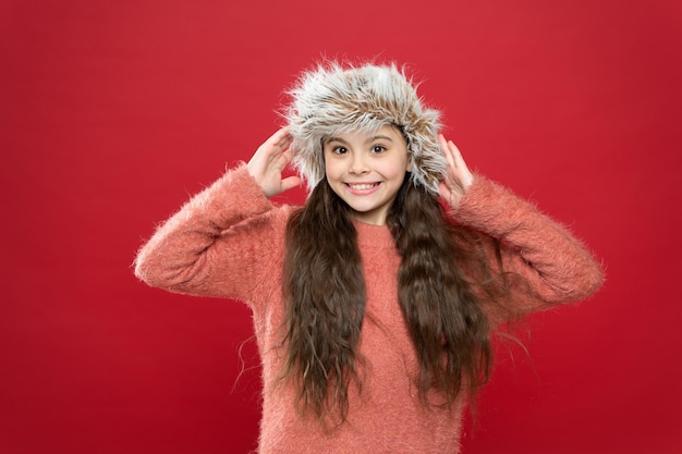 Niña linda en estilo invernal pared roja actividad de vacaciones al aire libre niño pequeño listo para el cuidado de la salud estacional de invierno moda infantil Ropa de abrigo y consejos para accesorios niña feliz con sombrero con orejeras