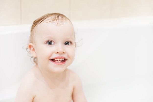 Niña linda feliz en el baño. Niño sonriente jugando con espuma.