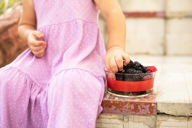 Niña linda feliz de comer frutas frambuesas y moras Comida deliciosa y saludable para niños