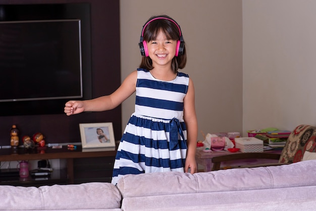 Niña linda feliz escuchando música en el sofá en casa.