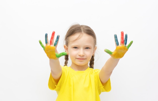 Niña linda feliz con manos pintadas de colores aisladas en un concepto de educación blanco