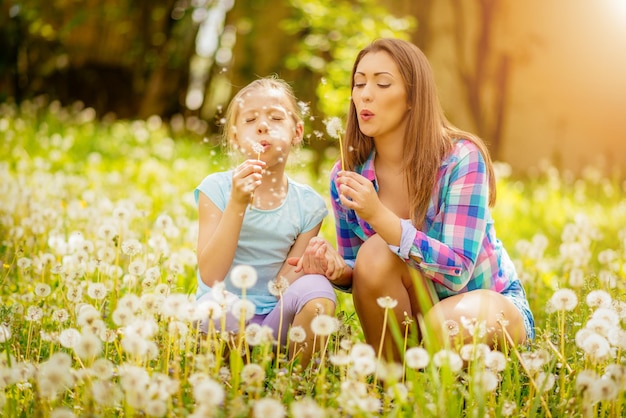 Niña linda feliz que sopla el diente de león con la madre en el parque.