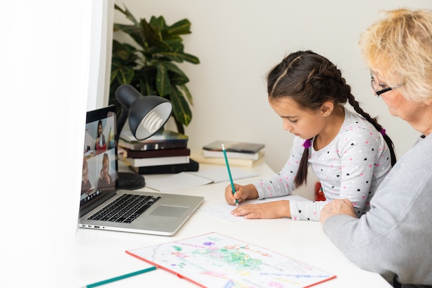 Foto niña linda y feliz que usa la computadora portátil con su abuela, estudiando a través del sistema de e-learning en línea.