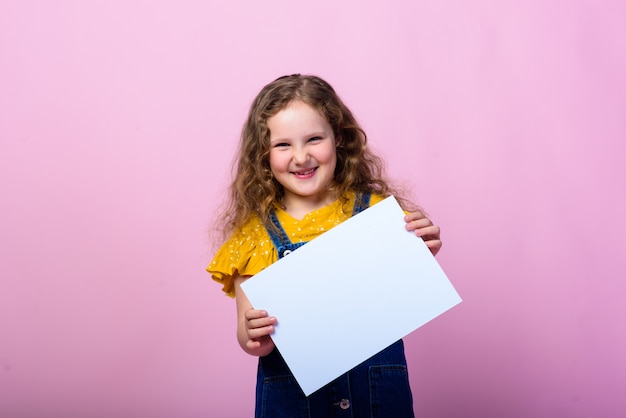 Niña linda con el fondo rosado blanco vacío de la hoja de papel