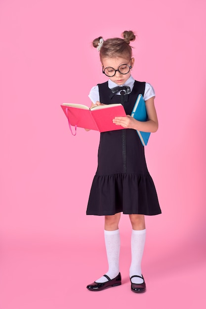 Niña linda con gafas y libros sobre espacio rosa, espacio para texto. Concepto de lectura