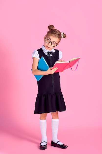 Niña linda con gafas y libros sobre fondo rosa