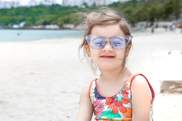 Una niña linda con gafas en la playa junto al mar. Entretenimiento y recreación de verano.