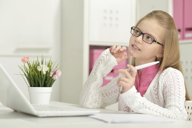 Niña linda en gafas con portátil y bolígrafo en casa