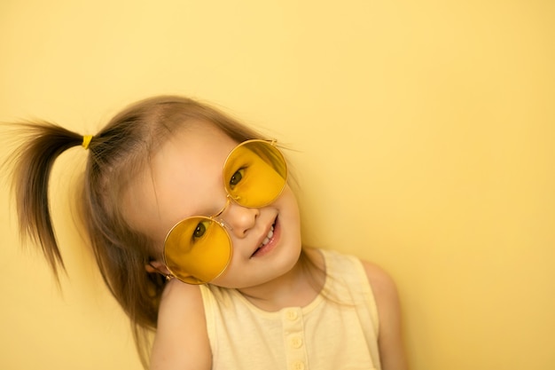 Una niña linda con gafas de sol sobre un fondo amarillo se ve con una sonrisa