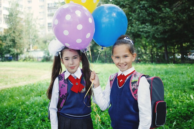 Niña linda con globos de colores cerca de la escuela en uniforme escolar