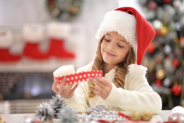 Niña linda con gorro de Papá Noel preparándose para Navidad en casa