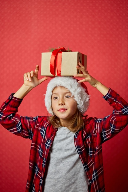 Niña linda con gorro de Papá Noel con un regalo de Navidad en la cabeza