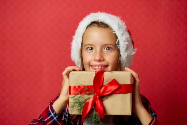 Niña linda con gorro de Papá Noel con regalos de Navidad delante de su cara