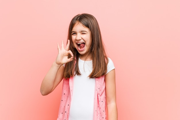 Niña linda guiña un ojo y tiene un gesto bien con la mano.