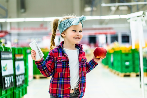 Niña linda haciendo una lista de productos para comprar en el supermercado