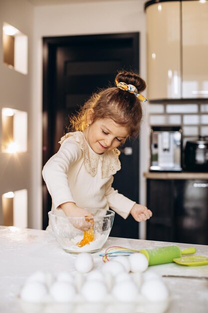 Niña linda haciendo masa de harina y huevos en un bol