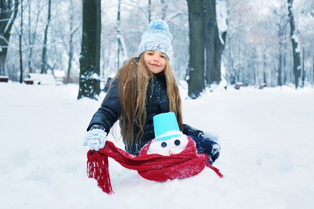 Niña linda haciendo muñeco de nieve en el parque de invierno